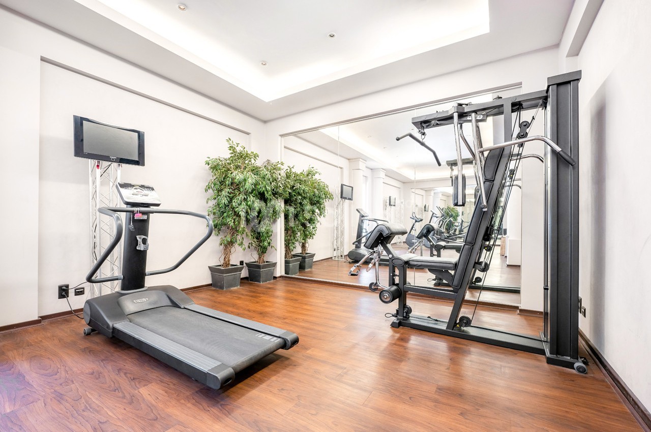 Salle de sport avec tapis de course, machine de musculation, miroir mural et plantes décoratives.