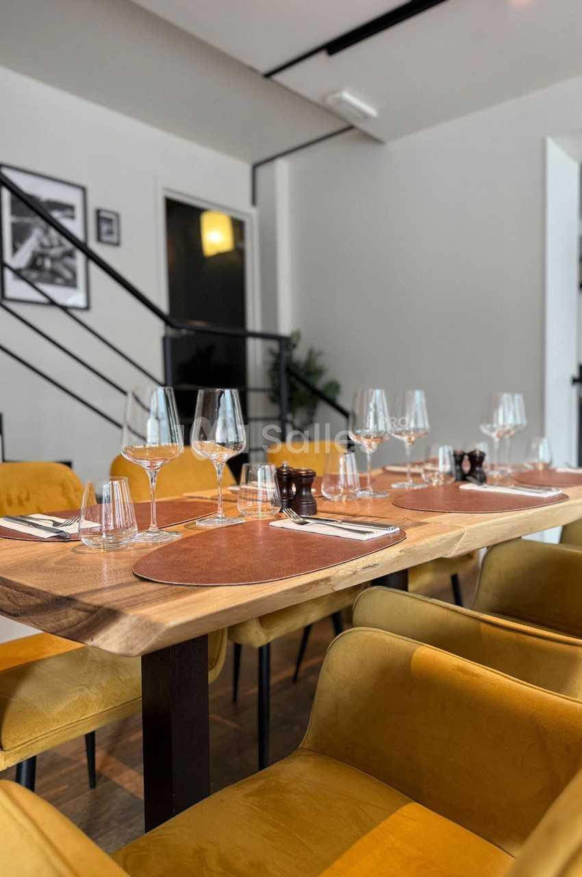 Salle de restaurant moderne avec tables en bois, chaises jaunes, verres et couverts disposés pour un repas.
