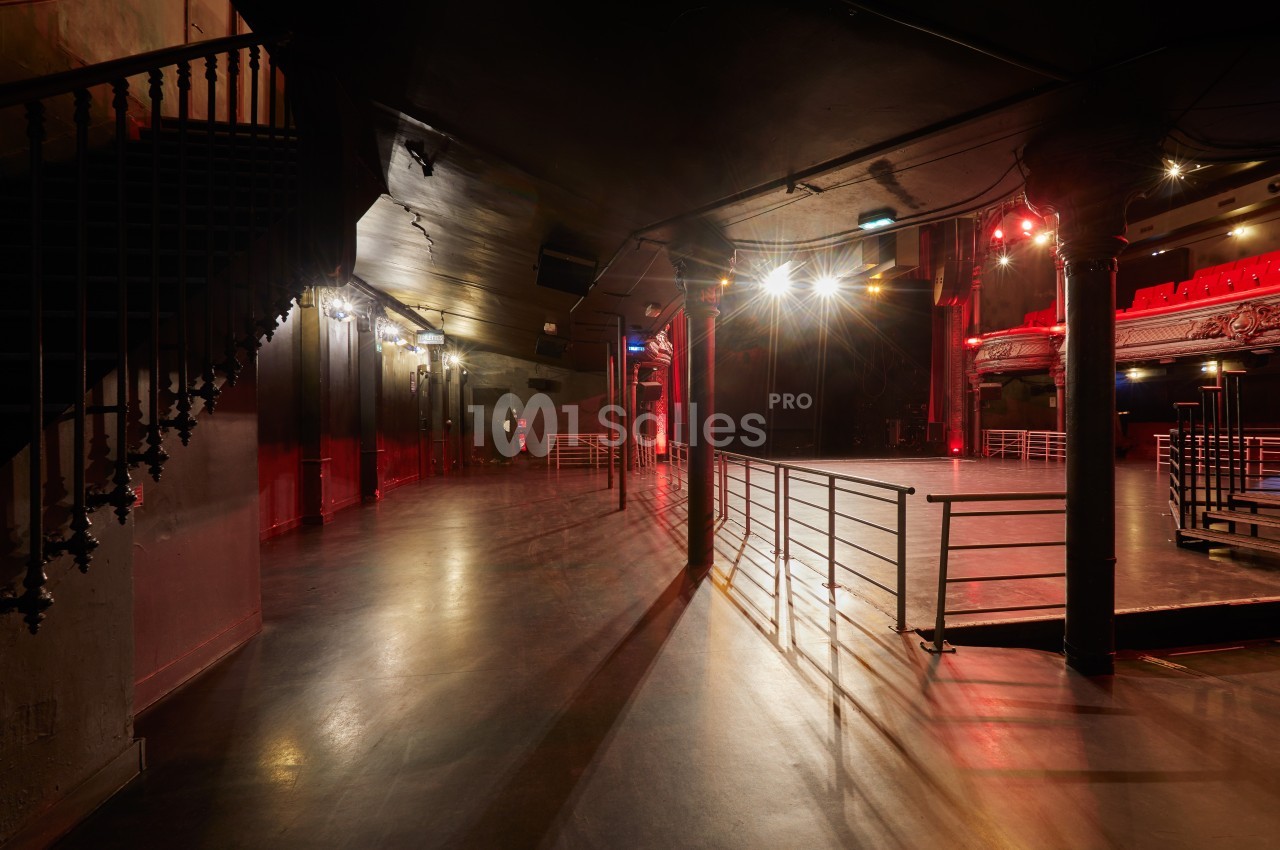 Salle de spectacle vide avec éclairage tamisé, balustrades métalliques et escalier en colimaçon à gauche.