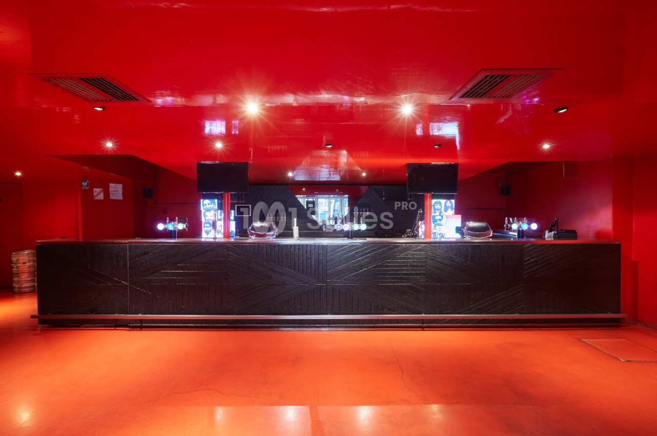 Comptoir de bar moderne en bois sombre dans une pièce aux murs et plafond rouges avec éclairage tamisé.