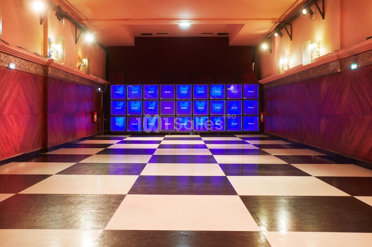 Salle vide avec sol à damier noir et blanc, murs rouges et un mur d'écrans bleus illuminés au fond.