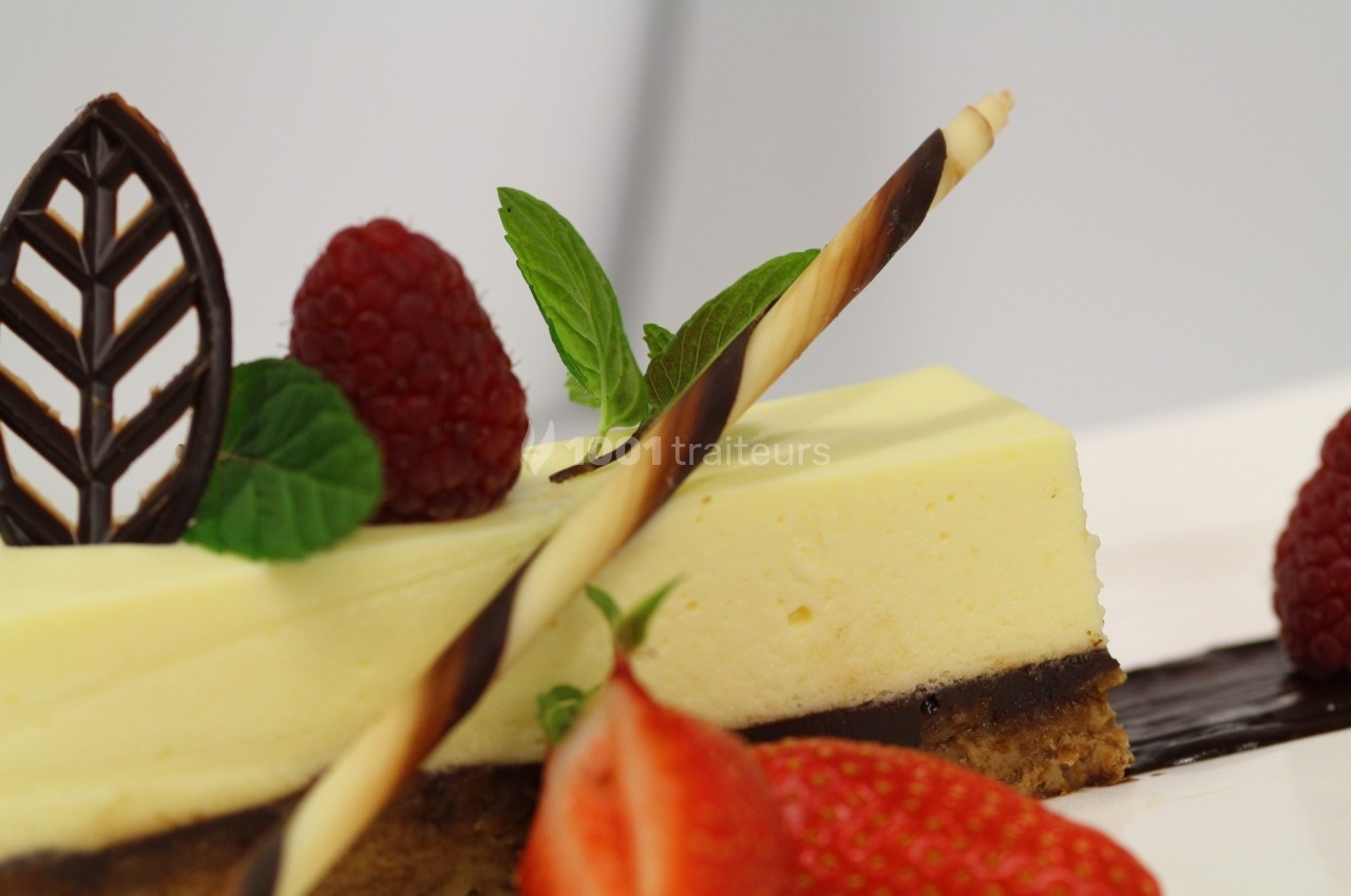 Part de gâteau au citron surmontée de framboises, feuilles de menthe, chocolat décoratif et fraise en garniture.