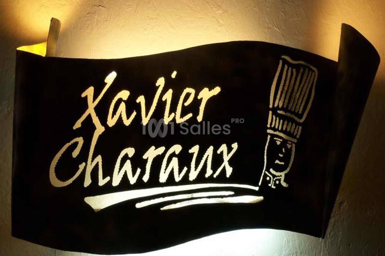 Enseigne en métal noir avec le texte ’Xavier Charaux’ et une illustration de toque de chef éclairée.