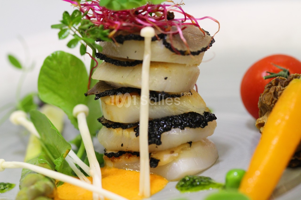 Assiette gastronomique avec des noix de Saint-Jacques, truffes, légumes colorés et sauce orange.