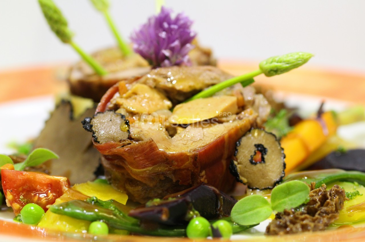 Plat gastronomique composé de viande enroulée, légumes colorés, truffes et asperges, présenté avec finesse.