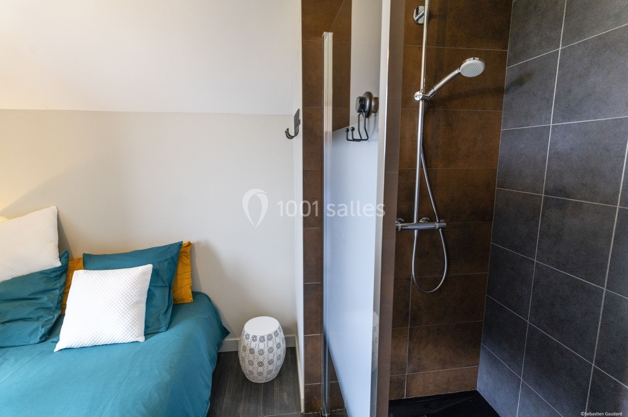 Chambre avec lit double, coussins colorés, lampe décorative et douche attenante avec carrelage sombre.
