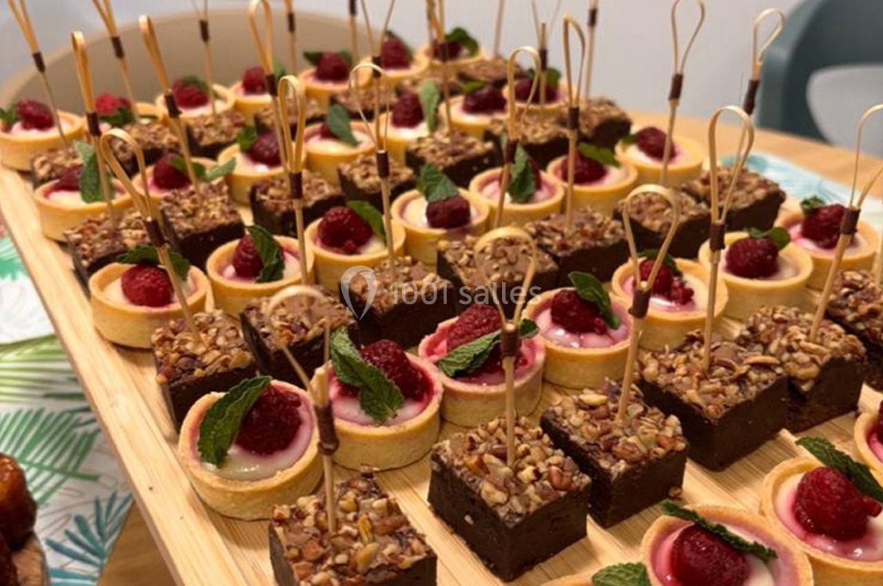 Plateau de mignardises composé de tartelettes aux framboises et de carrés au chocolat garnis de noix.