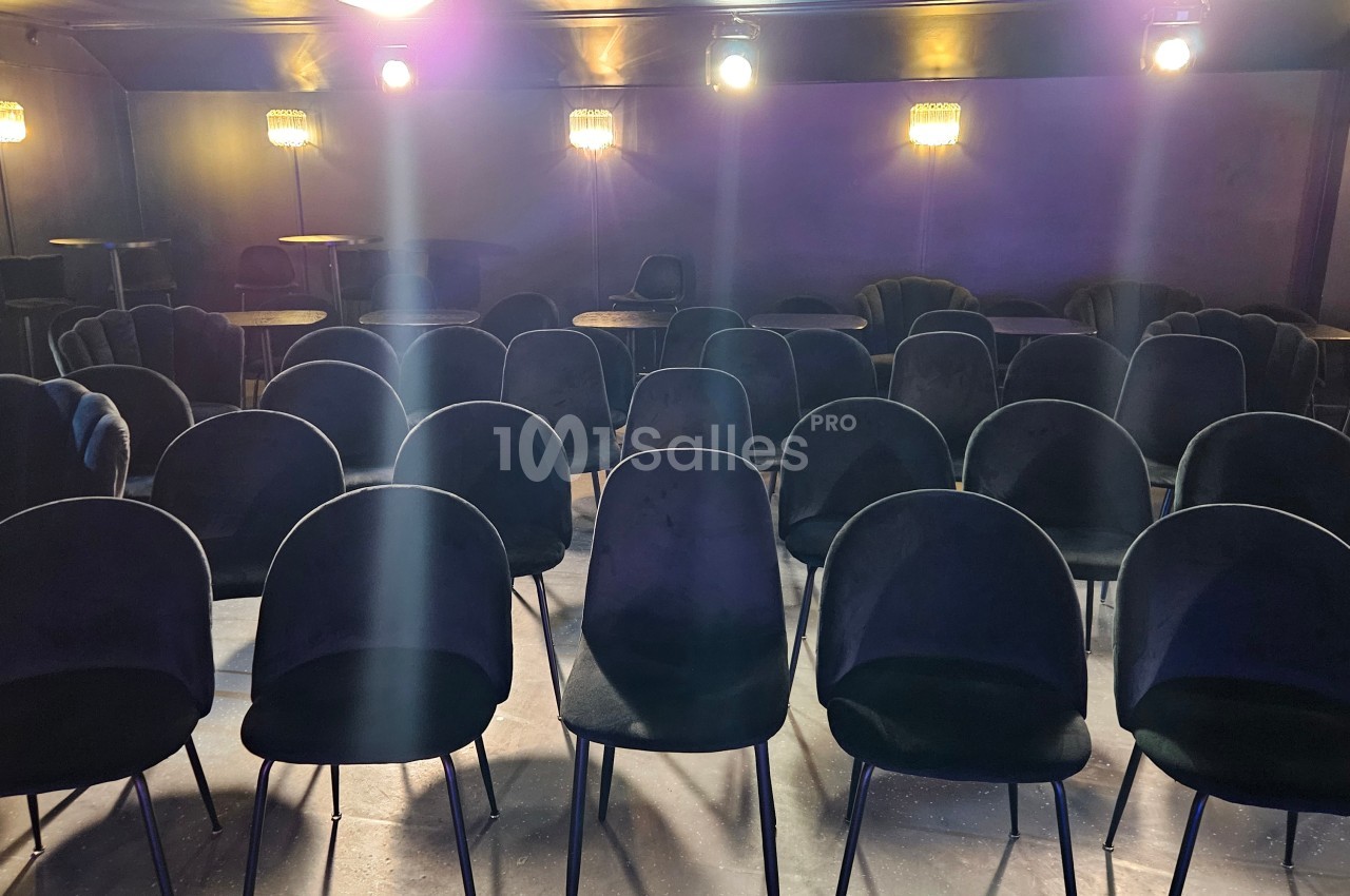 Salle vide avec des rangées de chaises noires alignées sous un éclairage tamisé.