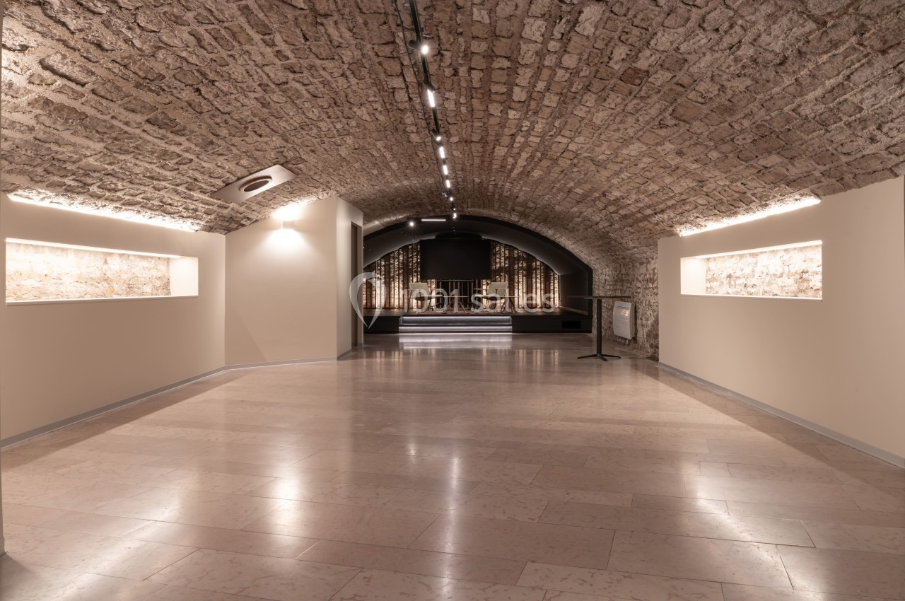 Salle voûtée en pierre avec éclairage intégré, murs clairs et espace aménagé pour des expositions ou événements.