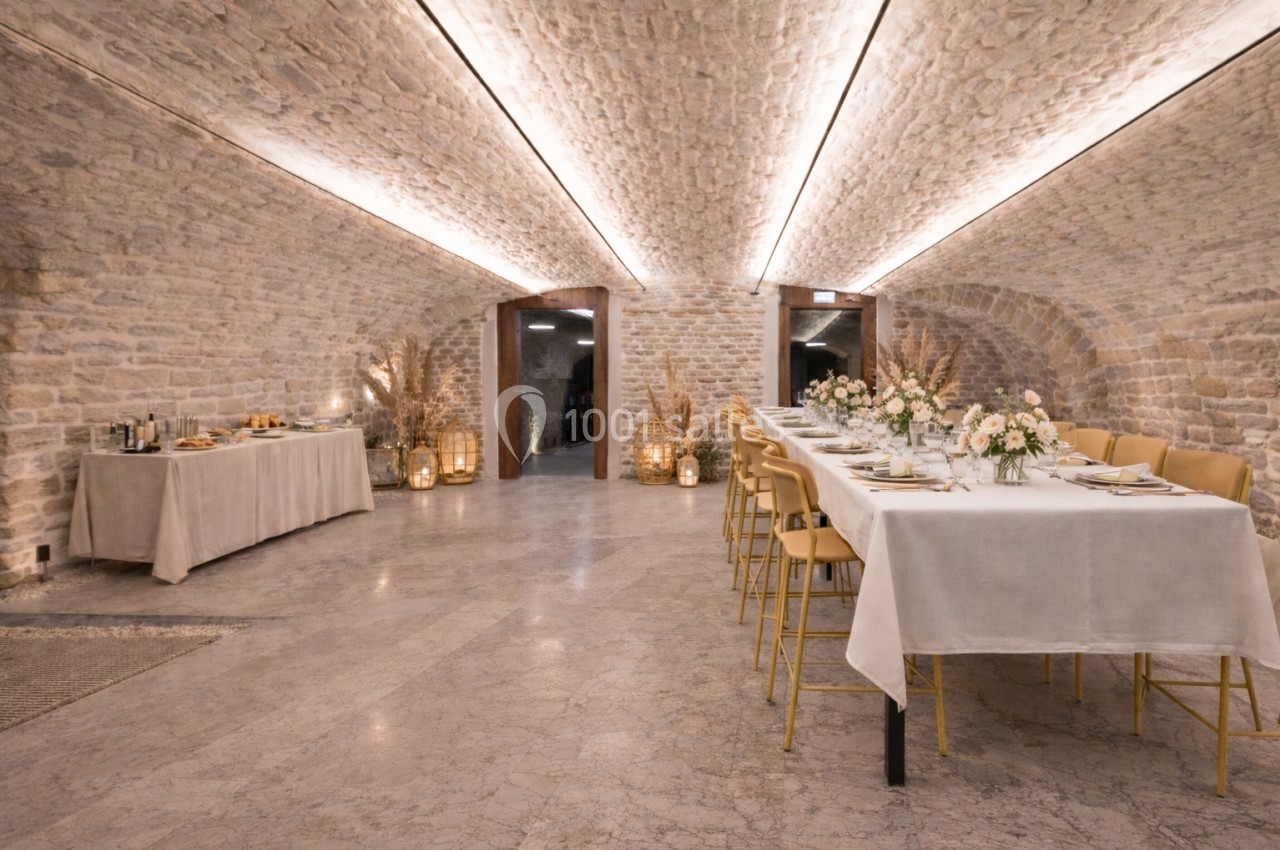 Salle voûtée en pierre avec tables décorées pour un repas, éclairage chaleureux et buffet en arrière-plan.