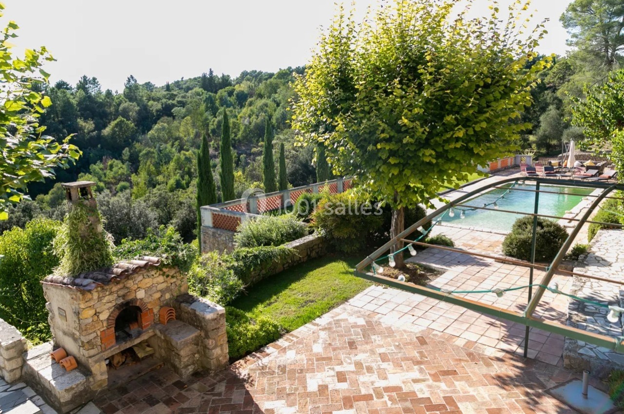 Jardin avec terrasse en briques, barbecue en pierre, piscine et vue sur une végétation dense et vallonnée.