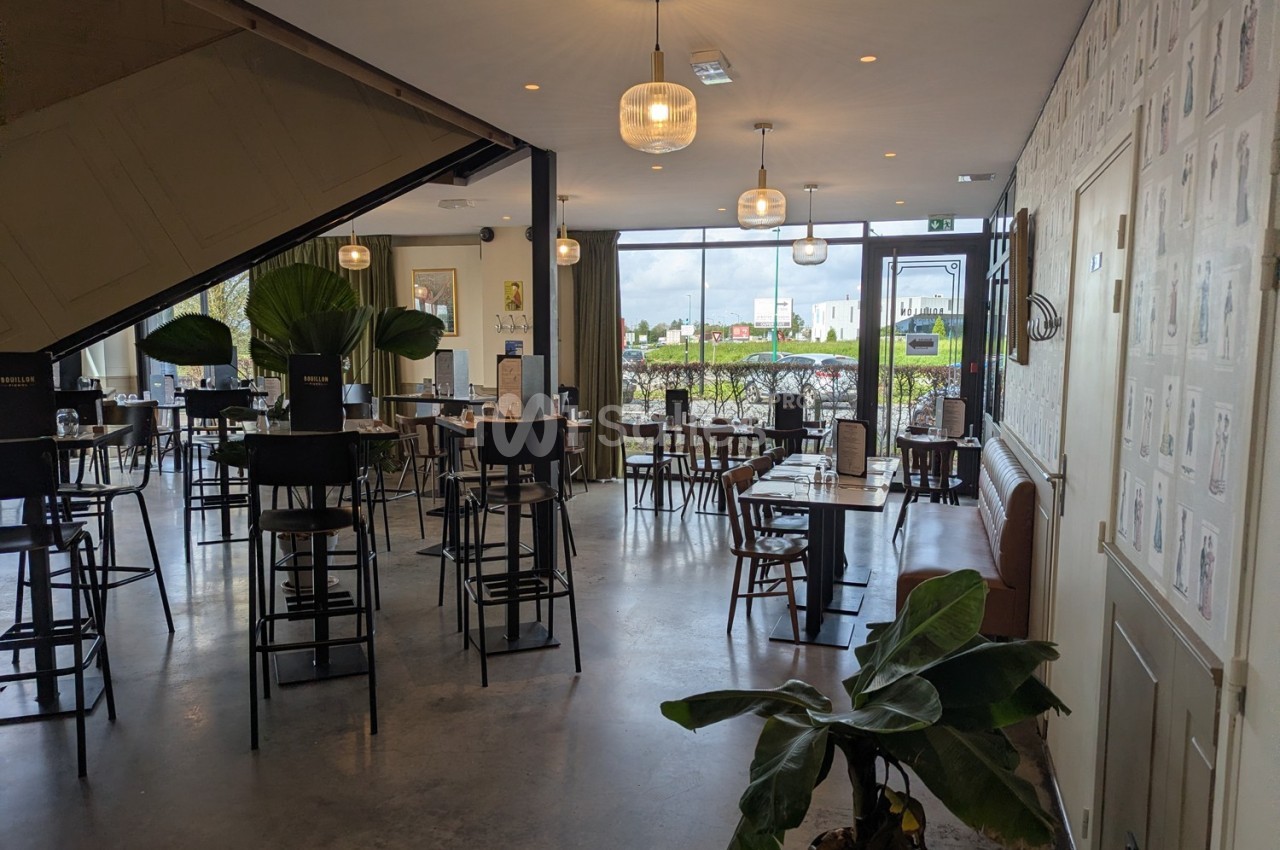 Salle de restaurant lumineuse avec tables et chaises, grandes baies vitrées donnant sur un extérieur verdoyant.