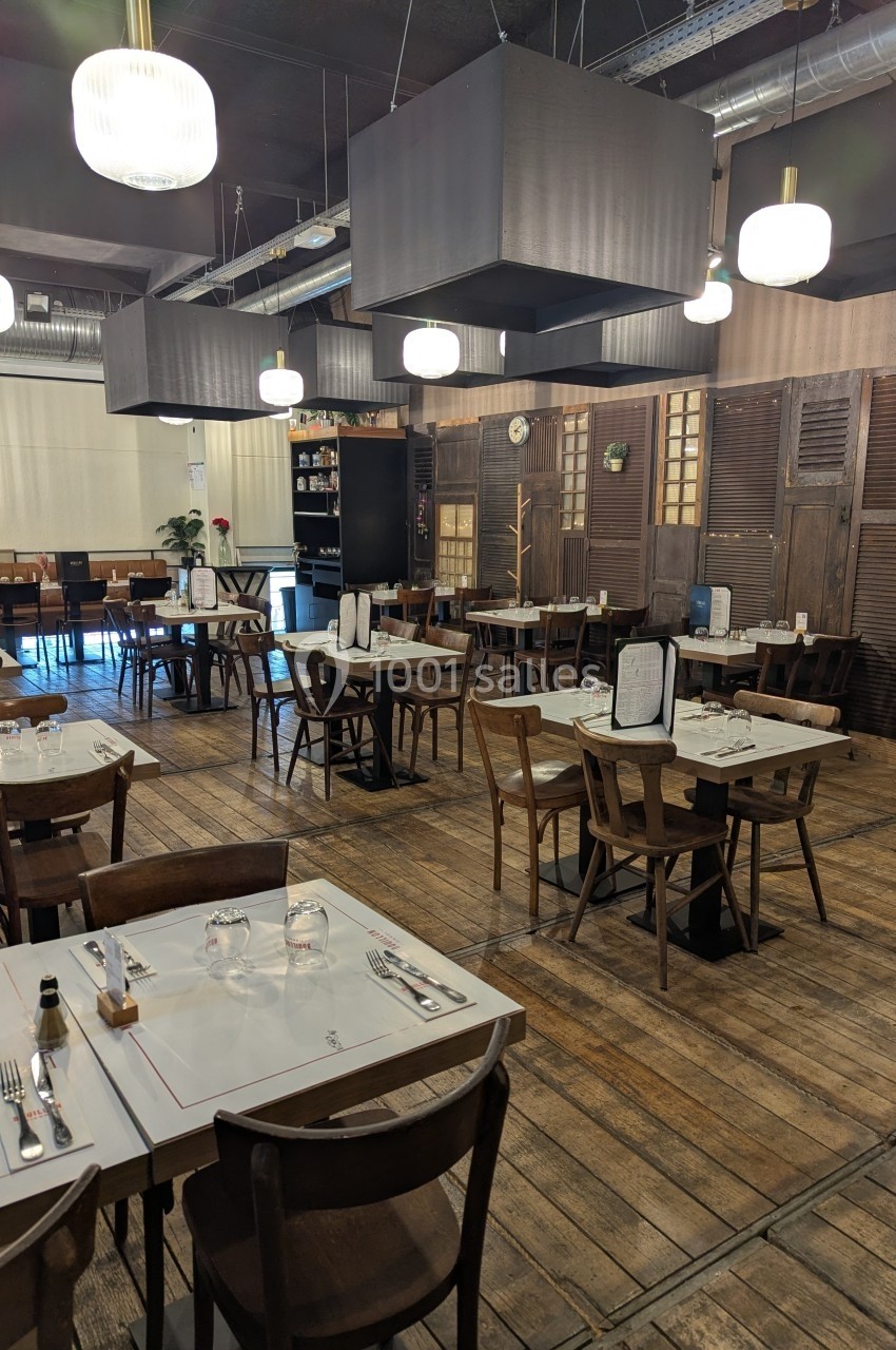 Salle de restaurant avec tables en bois dressées, éclairage suspendu et décoration intérieure chaleureuse.