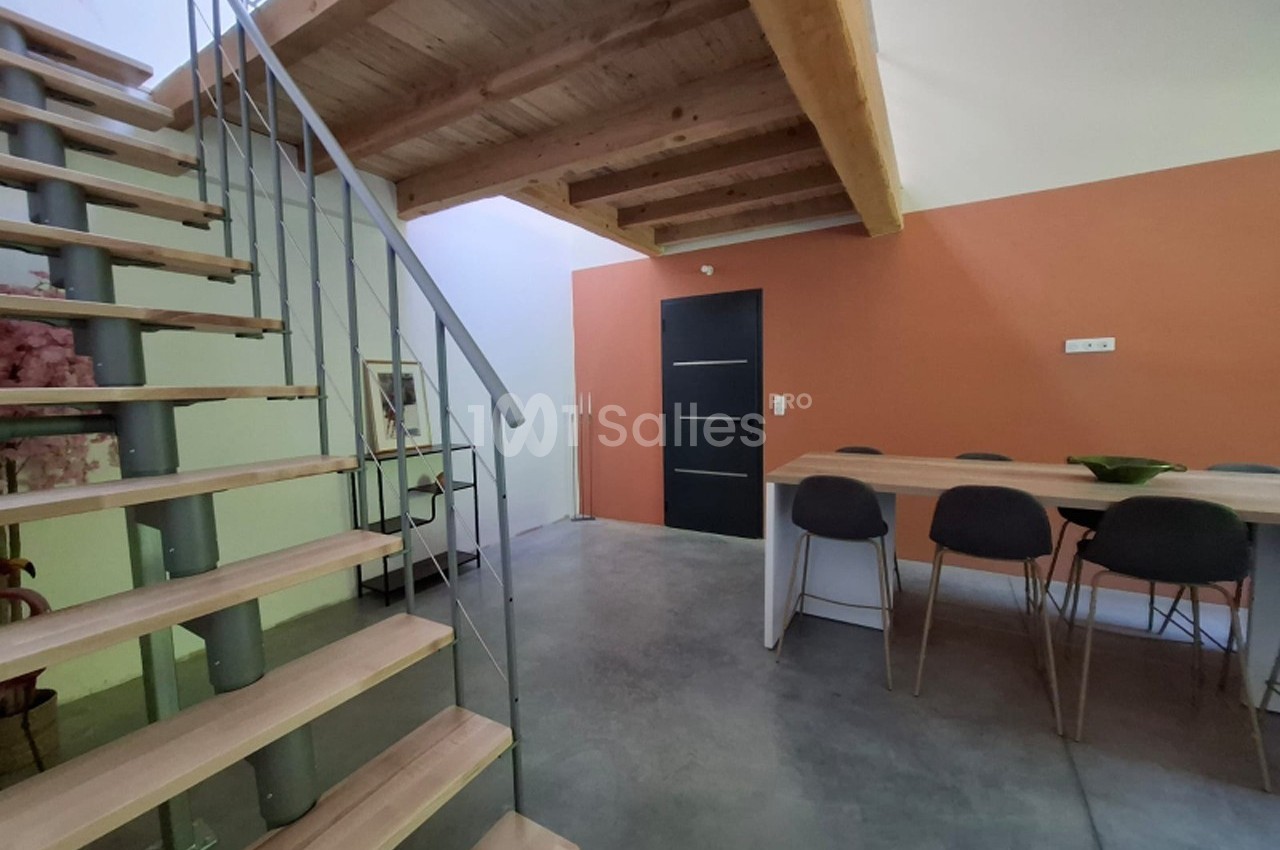 Escalier en bois et métal menant à une mezzanine, avec une table et des chaises dans un espace à mur orange.