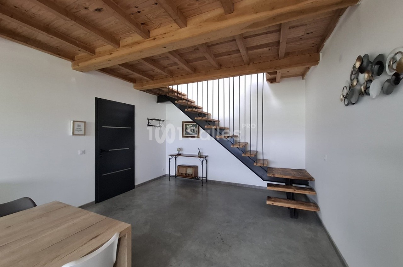Escalier en bois et métal dans un salon moderne avec plafond en poutres apparentes et sol en béton ciré.