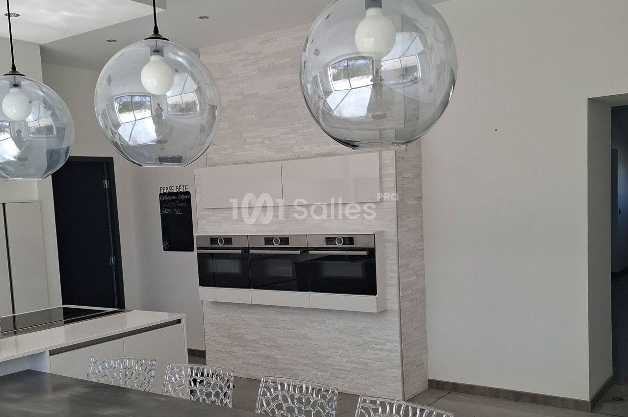Cuisine moderne avec des fours encastrés, un îlot central, des suspensions sphériques et des chaises design.