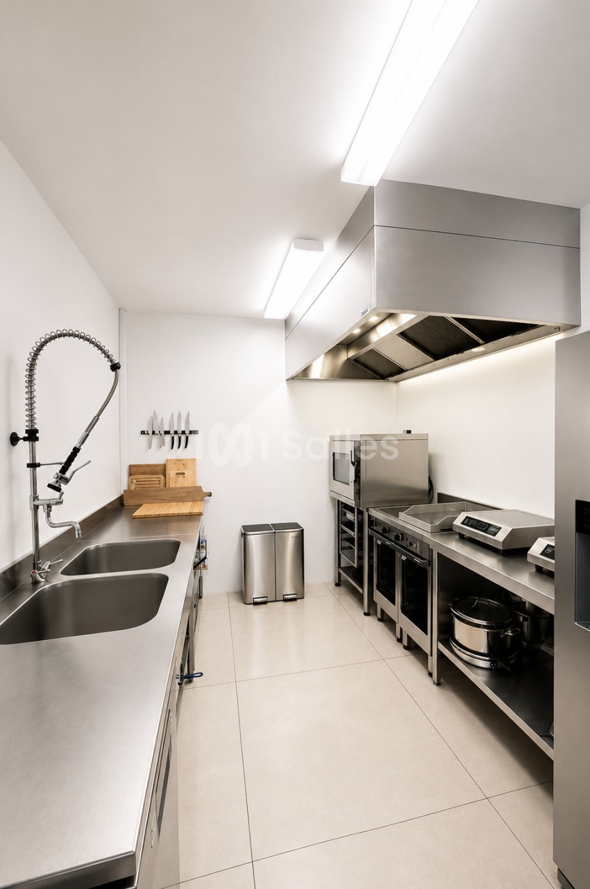 Cuisine professionnelle avec deux éviers inox, équipements de cuisson et plan de travail, éclairage zénithal.