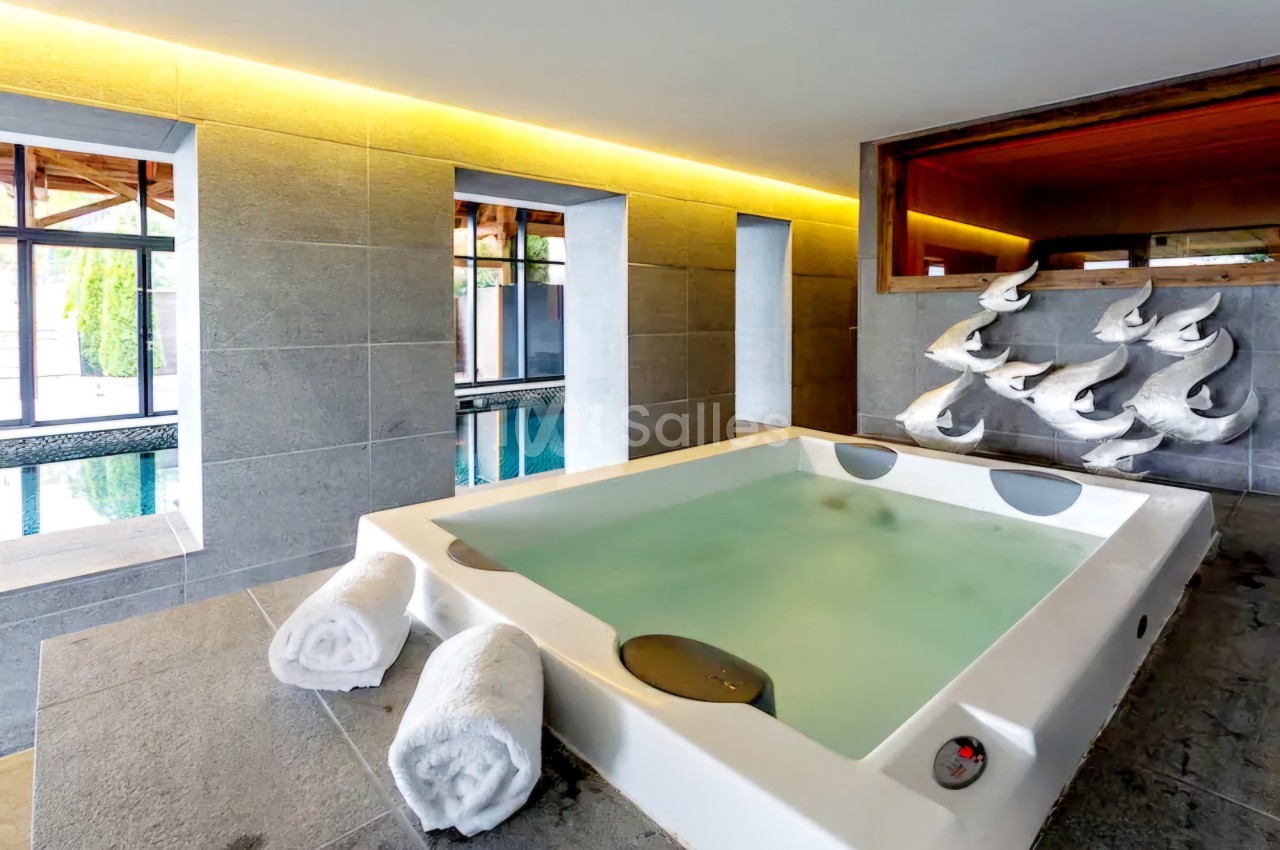 Espace spa intérieur avec bain à eau verte, serviettes blanches roulées, baie vitrée sur piscine et décor mural en poissons blancs.