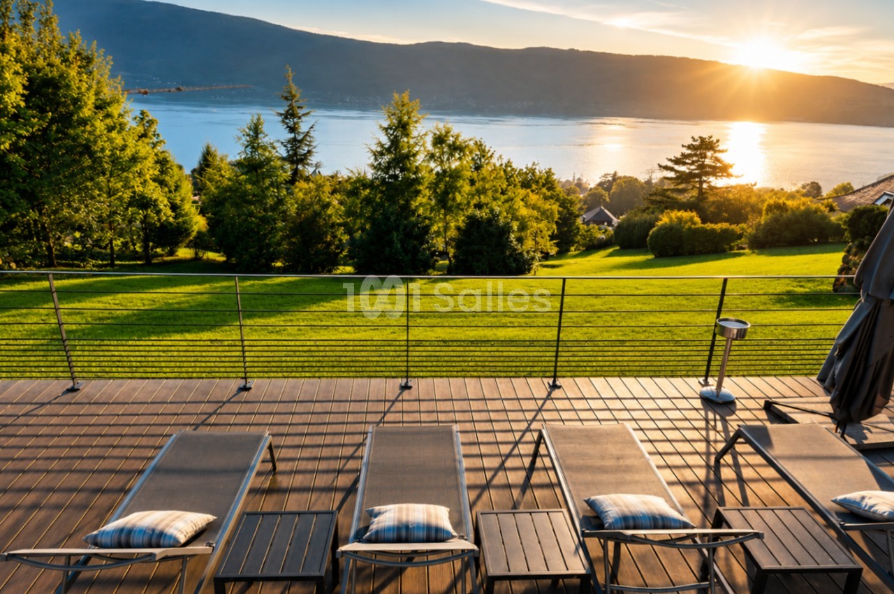 Terrasse en bois avec transats face à un lac et montagnes au coucher de soleil.