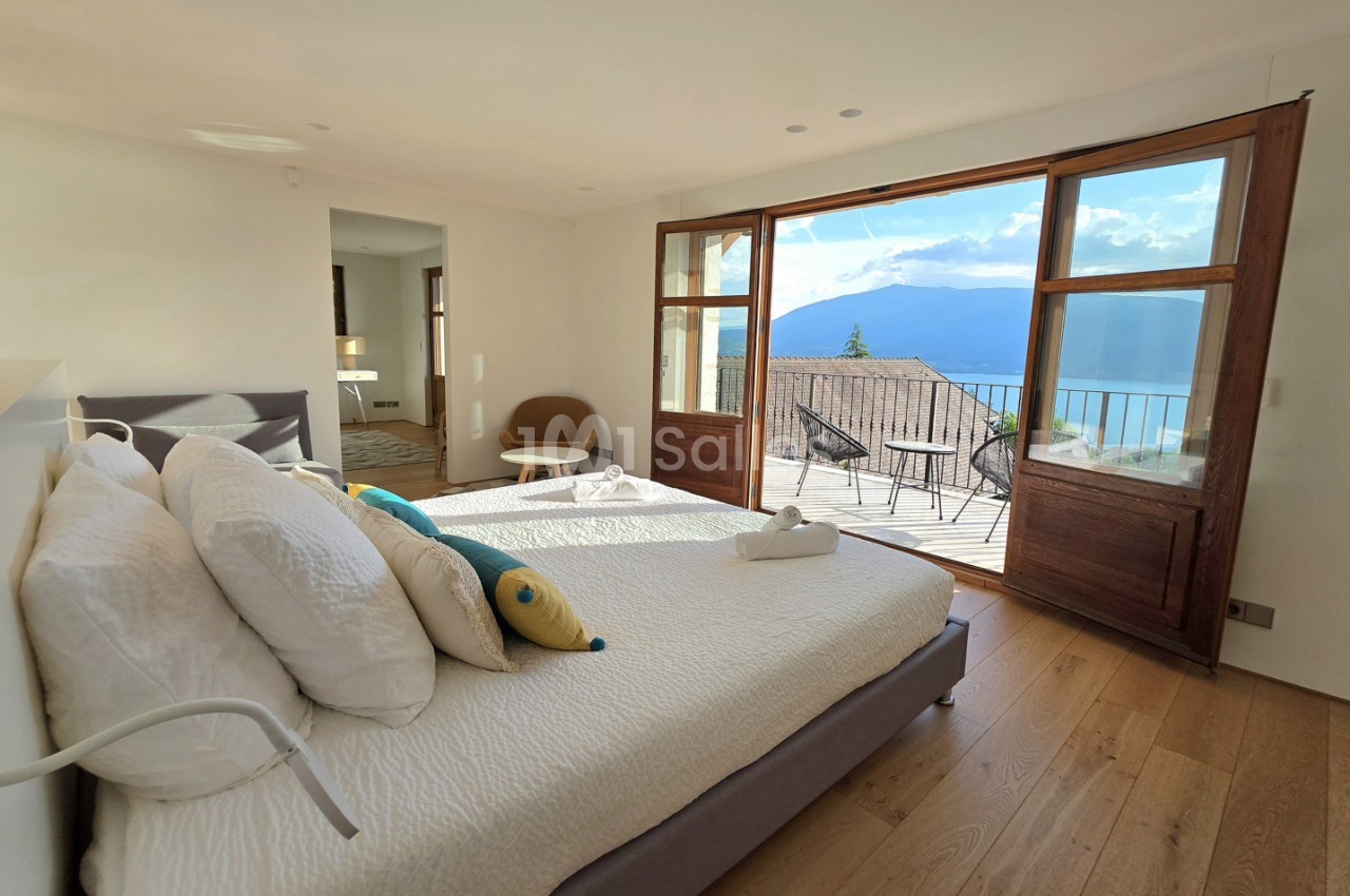 Chambre avec lit double, baies vitrées coulissantes ouvrant sur terrasse et vue panoramique sur lac et montagne.