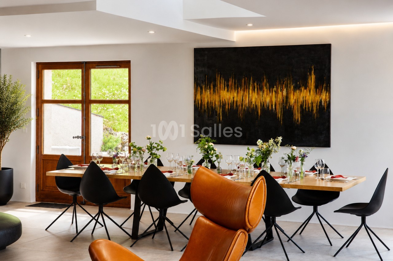 Salle de réception moderne avec table en bois, chaises noires et orange, fleurs fraîches et verrerie.