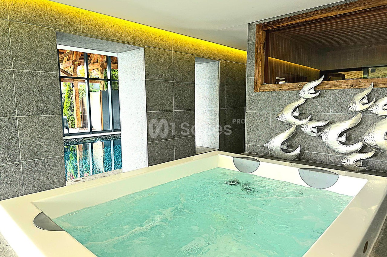 Bain à remous dans une pièce moderne avec murs en pierre grise, vue sur une piscine et sculptures murales décoratives.