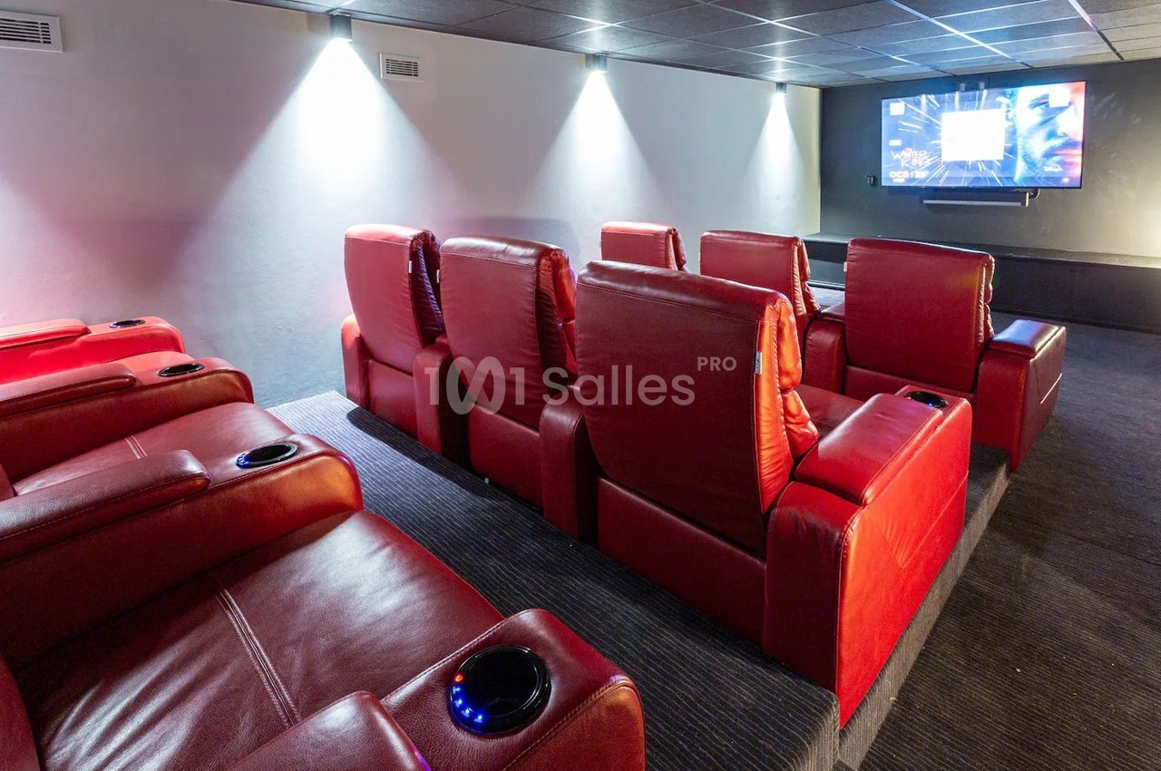 Salle de cinéma privée avec fauteuils rouges inclinables et écran de projection allumé sur un mur blanc.