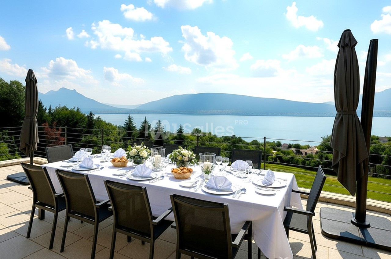 Table dressée en extérieur avec vue sur un lac et des montagnes, entourée de parasols fermés et de verdure.