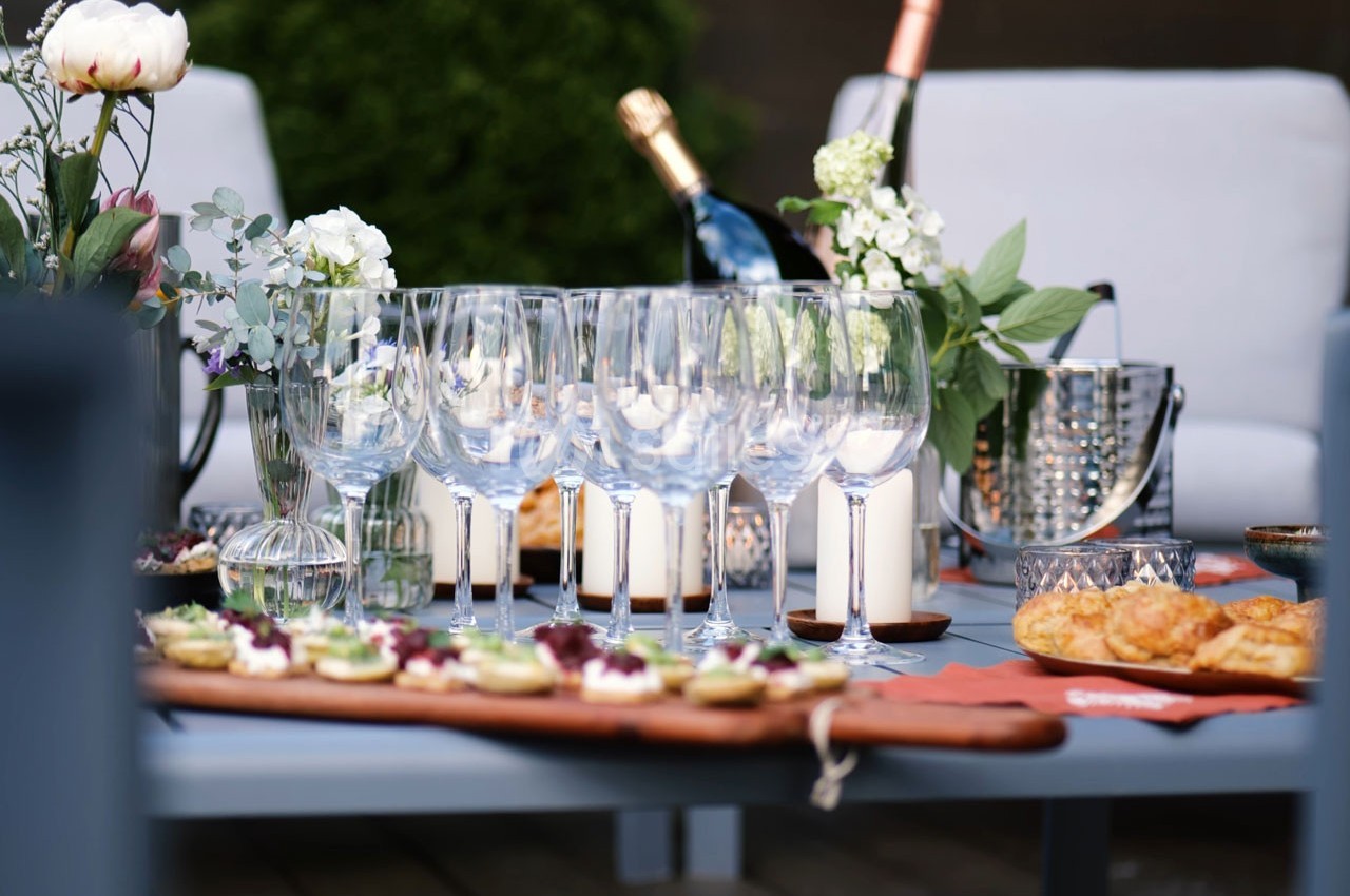 Table extérieure dressée avec des verres à vin, des fleurs, des bougies et des plateaux de nourriture.
