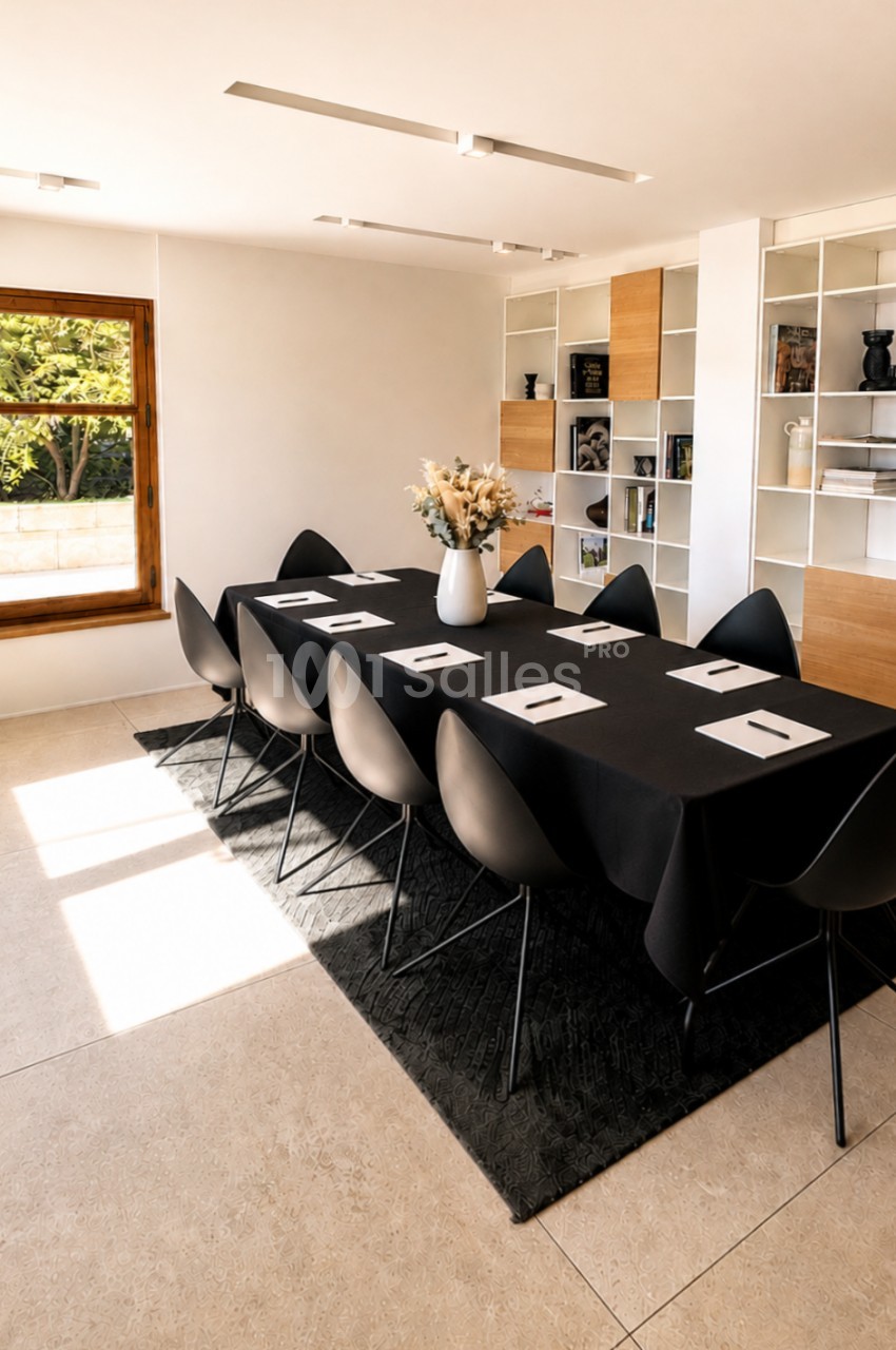 Salle de réunion épurée avec table noire dressée pour 8 personnes, chaises bicolores et étagères modulables.