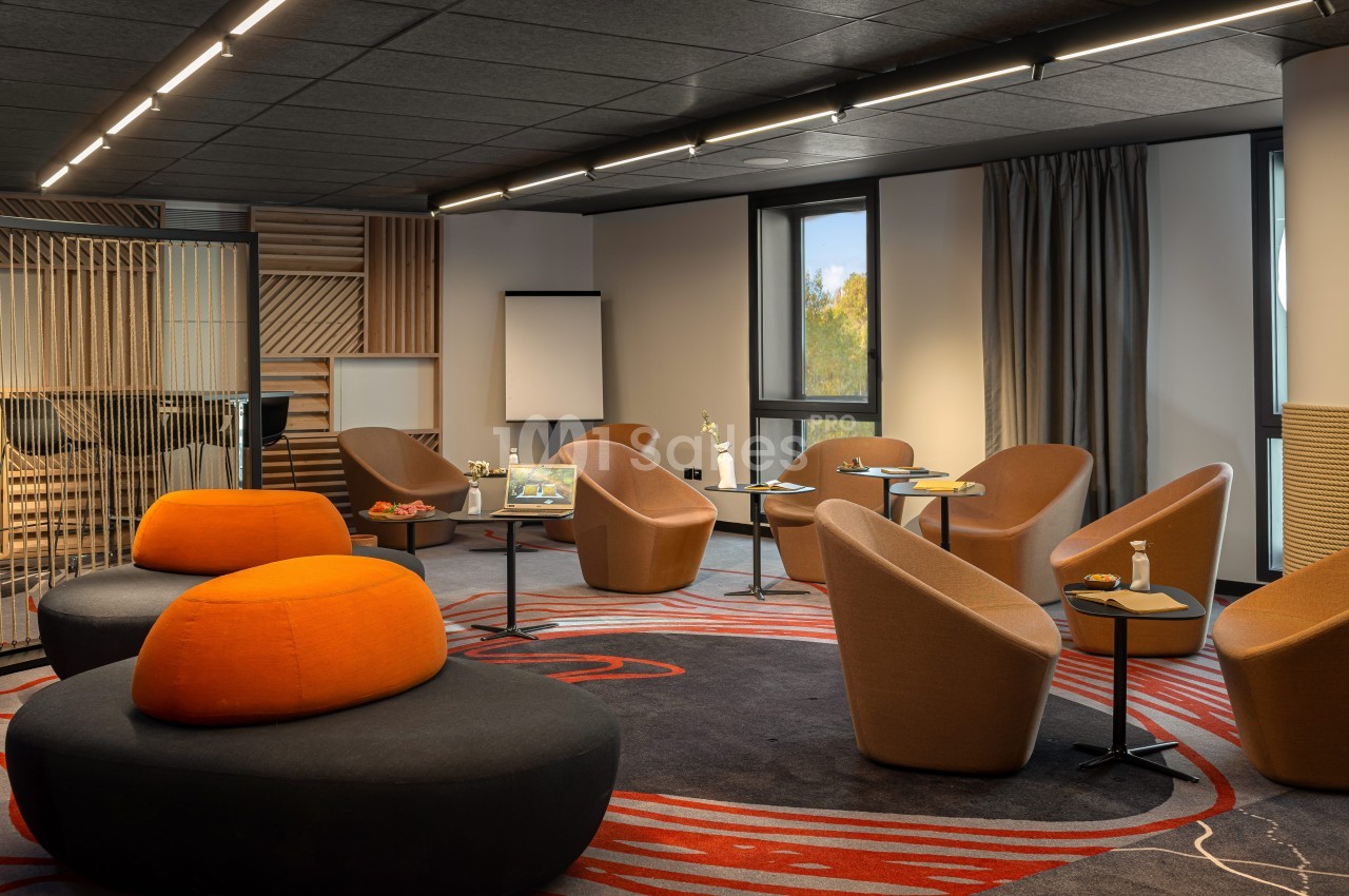 Salle de réunion moderne avec fauteuils, tables basses, tableau blanc et lumière naturelle.