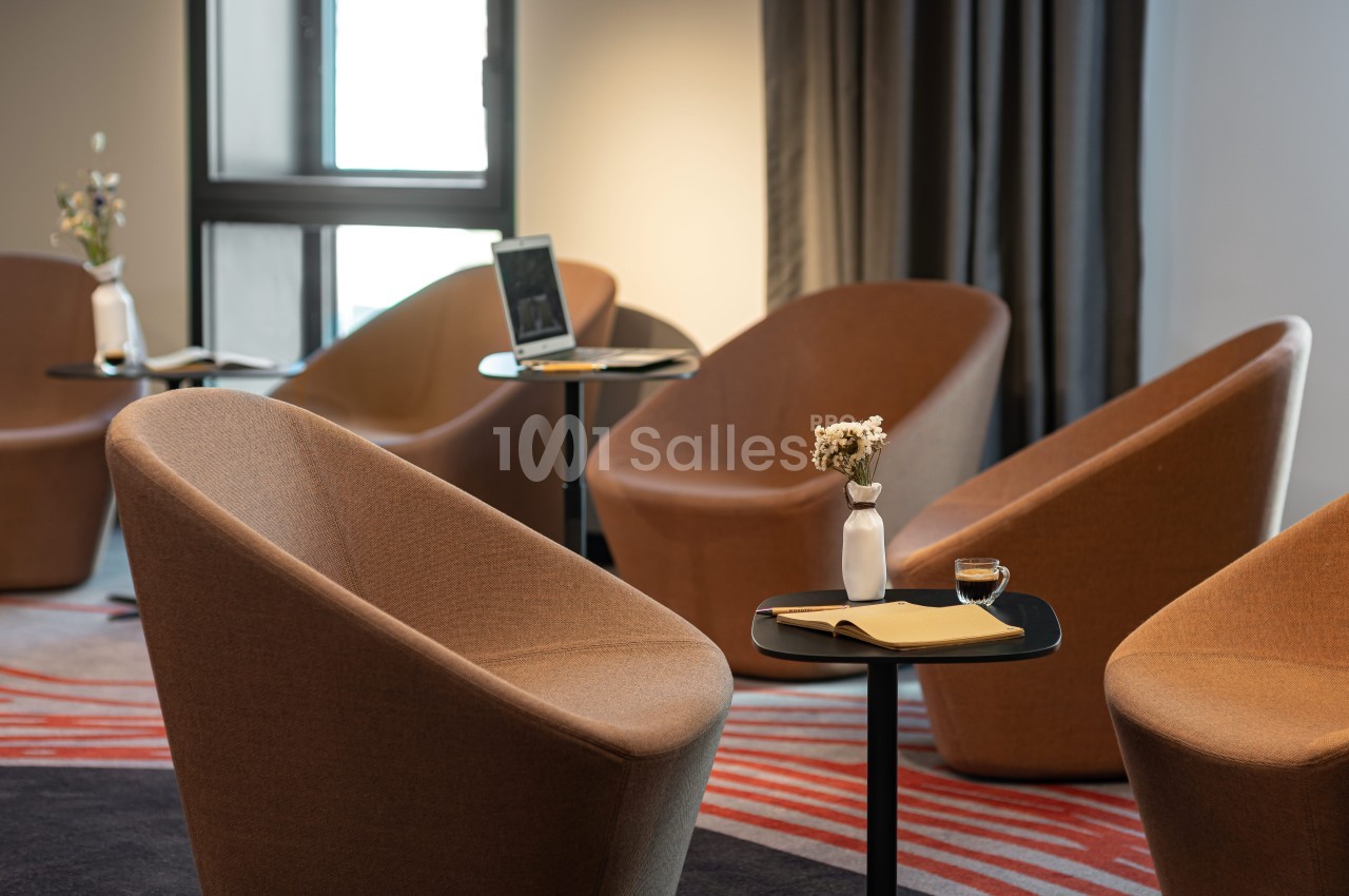 Salle avec fauteuils modernes, tables noires, carnets, fleurs en vase et lumière naturelle provenant d'une fenêtre.