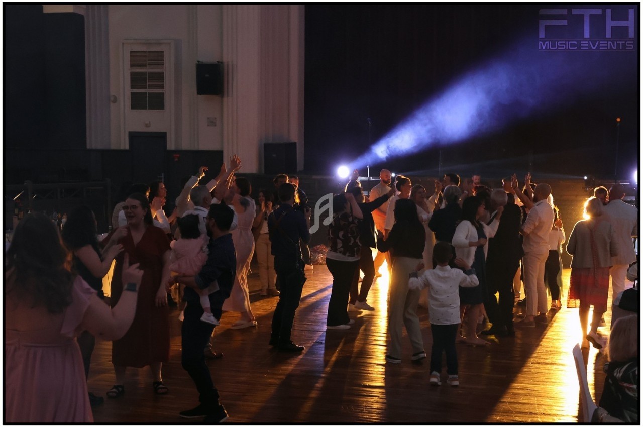 Groupe de personnes dansant dans une salle éclairée par des projecteurs, ambiance festive en soirée.