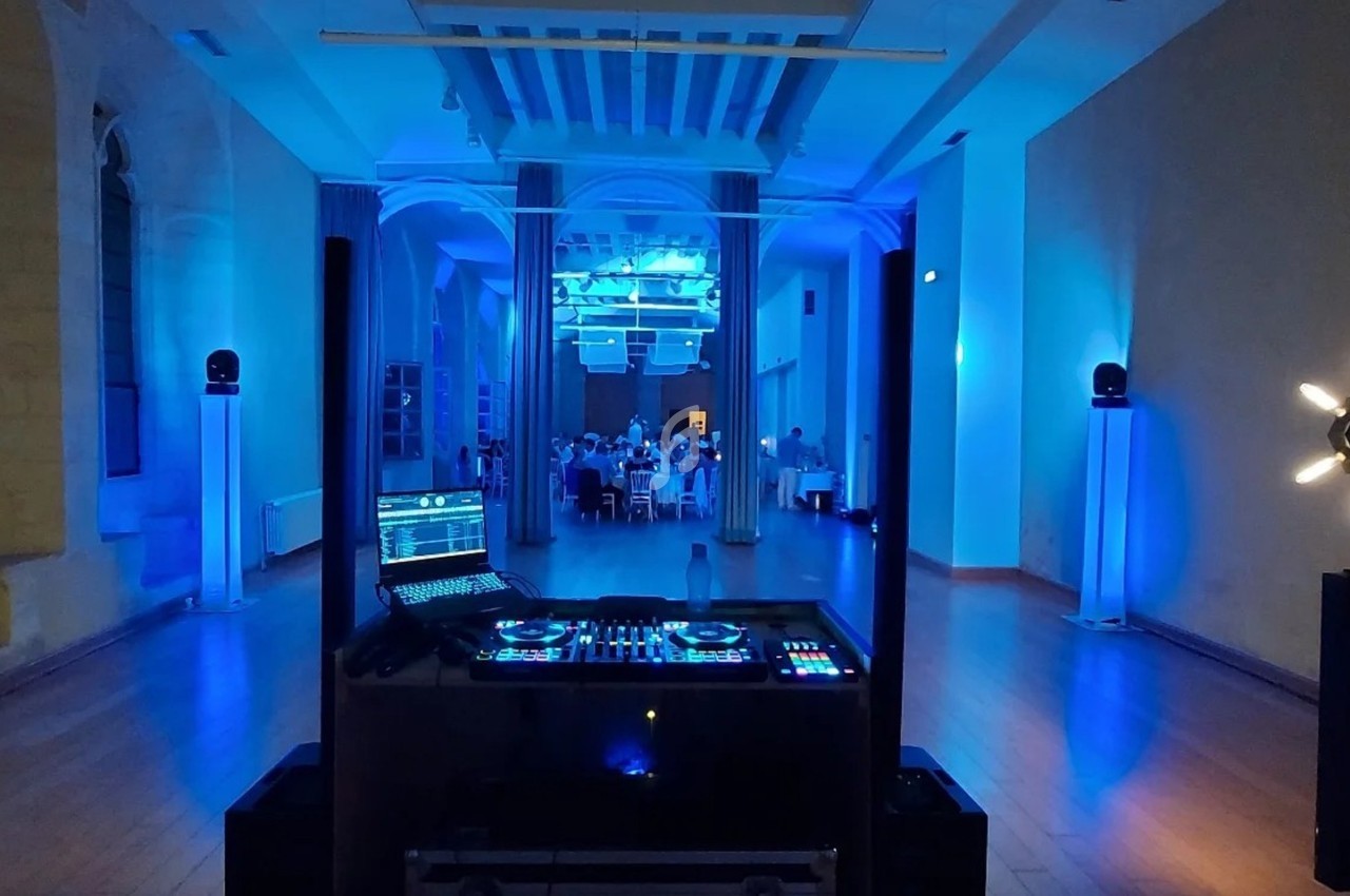 Salle éclairée en bleu avec une table de mixage au premier plan et des convives attablés en arrière-plan.