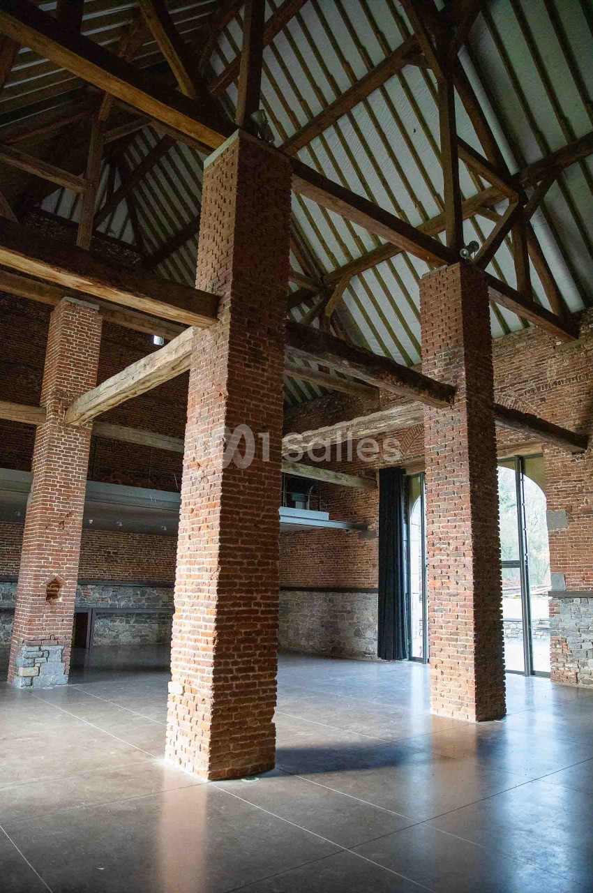 Intérieur d'une grande salle avec murs en briques, poutres apparentes et larges ouvertures vitrées.