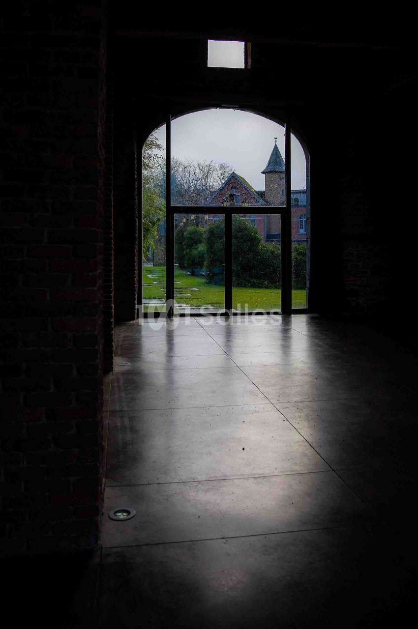 Vue d'un jardin verdoyant et d'une tour en pierre à travers une grande porte vitrée dans un bâtiment en briques.