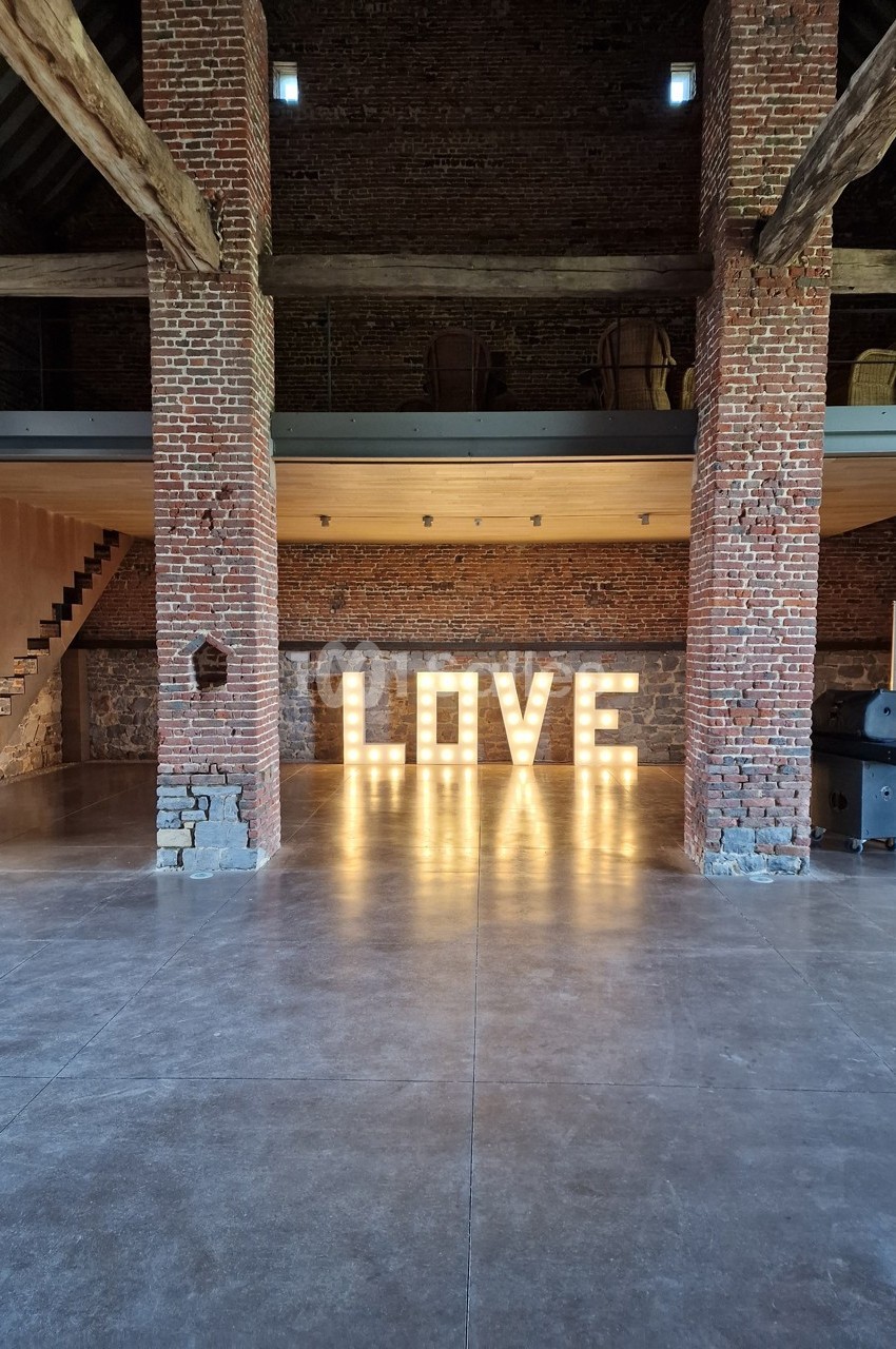 Grange en briques avec des lettres lumineuses formant le mot ’LOVE’ au centre de l'espace.