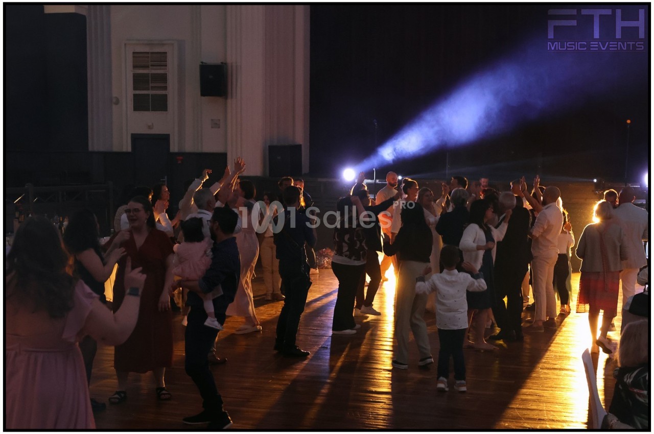Des personnes dansent et socialisent dans une salle éclairée par des projecteurs, créant une ambiance festive.