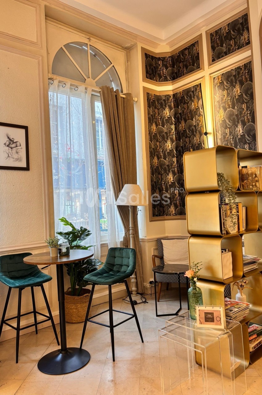 Coin salon lumineux avec chaises hautes vertes, table ronde, étagère dorée et décoration végétale près d'une fenêtre.