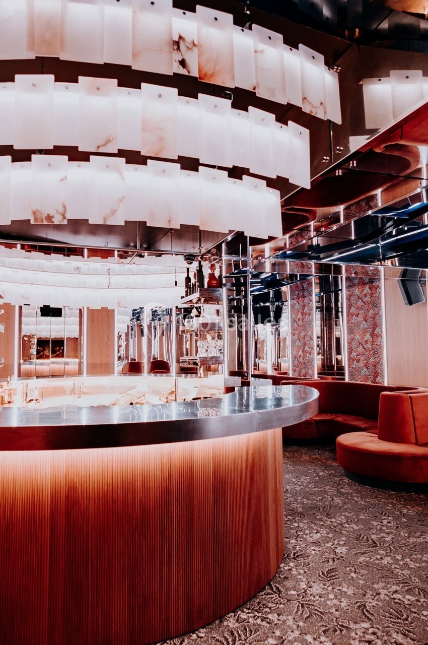 Intérieur d'un bar moderne avec comptoir incurvé, éclairage suspendu et banquettes rouges.