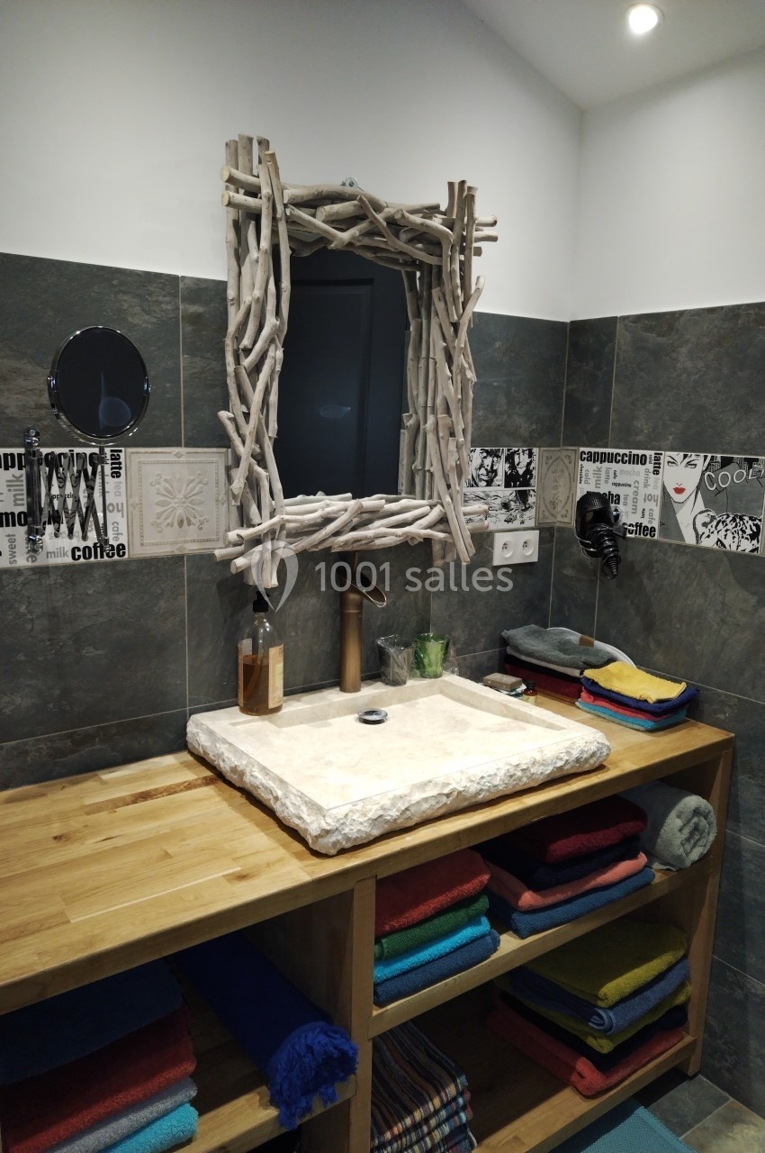 Lavabo en pierre sur meuble en bois avec miroir encadré de branches, dans une salle de bain aux murs en carrelage gris.