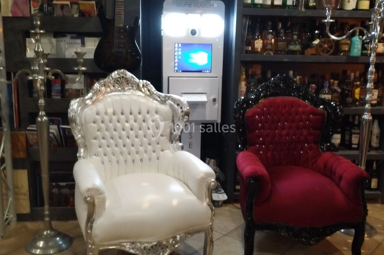 Deux fauteuils baroques, l'un blanc et l'autre rouge, devant un distributeur automatique dans un décor de bar.