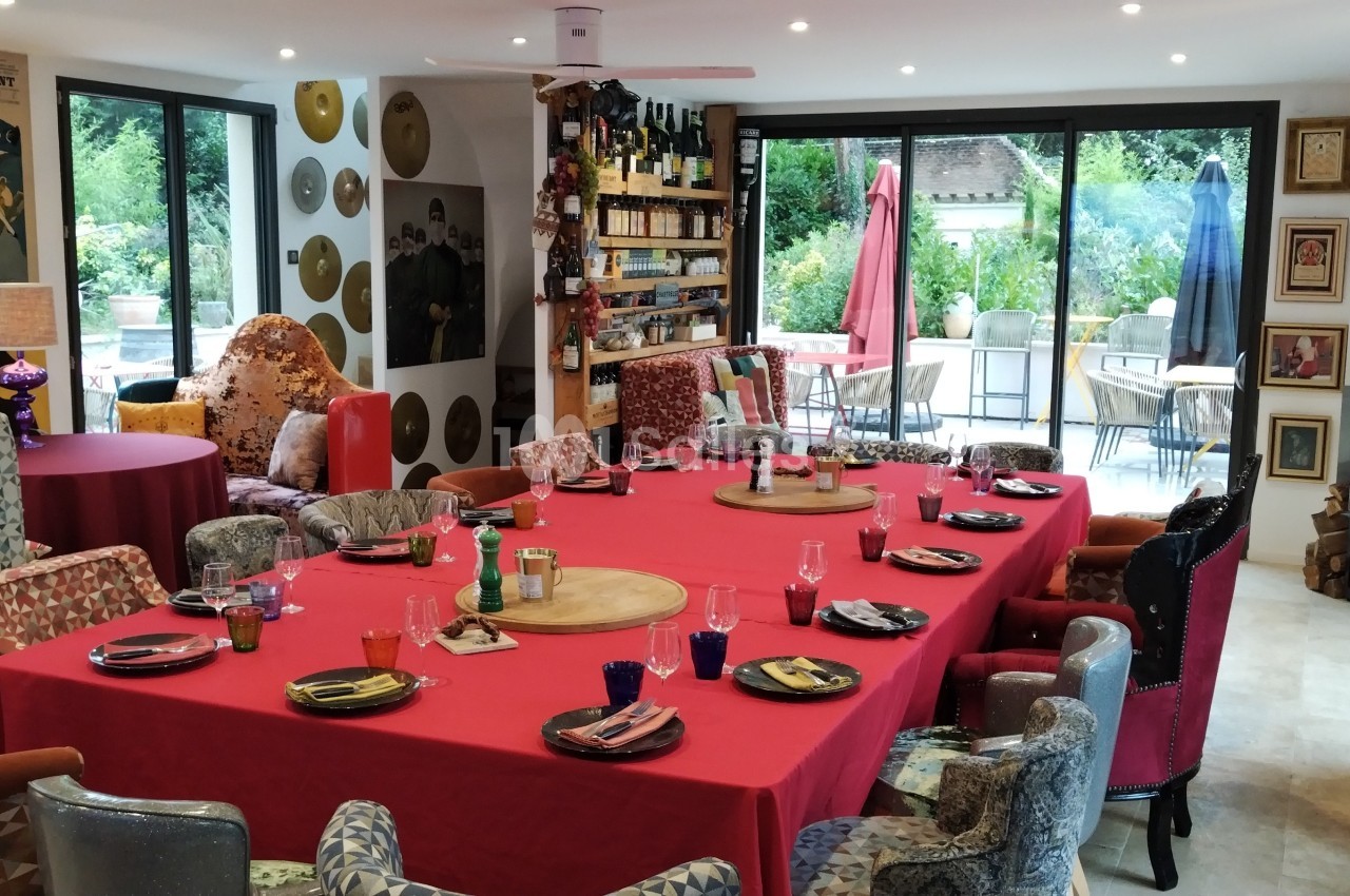 Salle à manger colorée avec une grande table dressée, entourée de fauteuils variés, donnant sur une terrasse verdoyante.