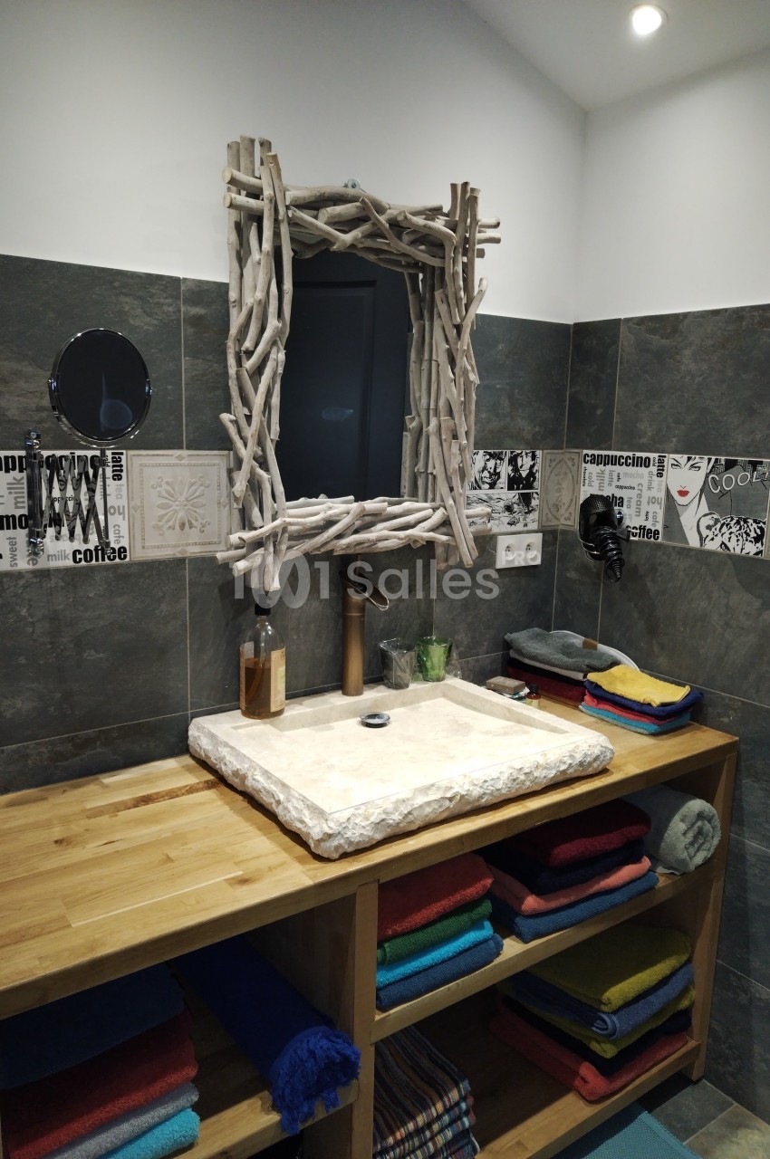 Meuble de salle de bain en bois avec vasque en pierre, miroir encadré de bois flotté et étagères garnies de serviettes…