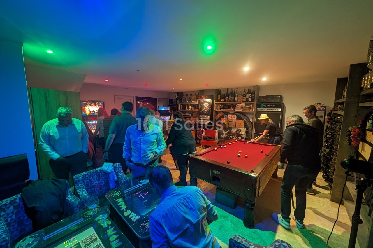 Personnes jouant au billard et à des jeux d'arcade dans une salle de loisirs éclairée par des lumières colorées.