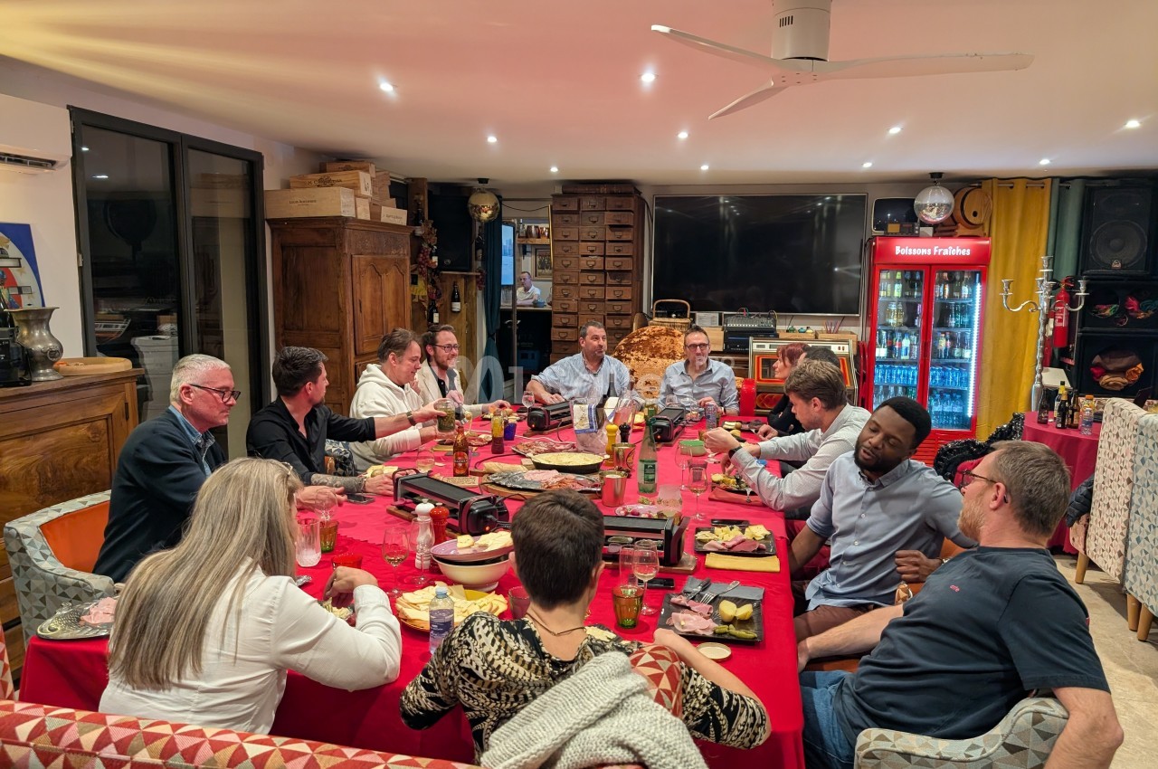 Groupe de personnes partageant un repas autour d'une grande table dans une salle chaleureuse et éclairée.
