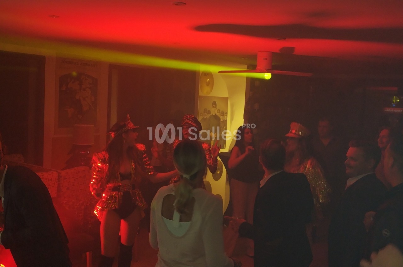 Personnes dansant et discutant dans une ambiance tamisée avec éclairage rouge lors d'une fête en intérieur.