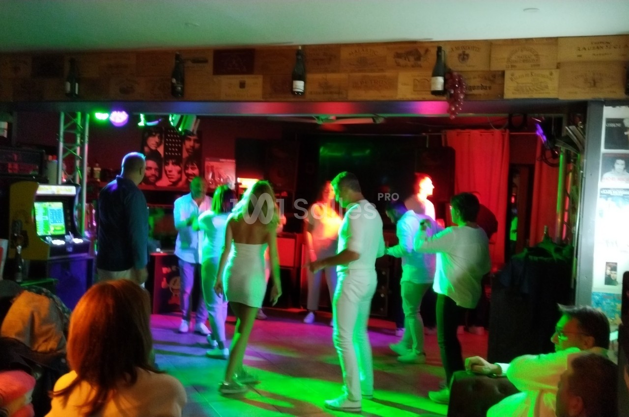 Des personnes dansent dans une salle éclairée par des lumières colorées, entourées de spectateurs assis.