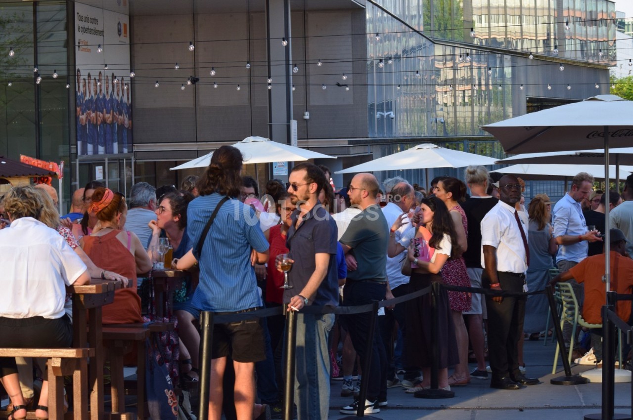 Groupe de personnes discutant et partageant des boissons en terrasse sous des parasols par une journée ensoleillée.