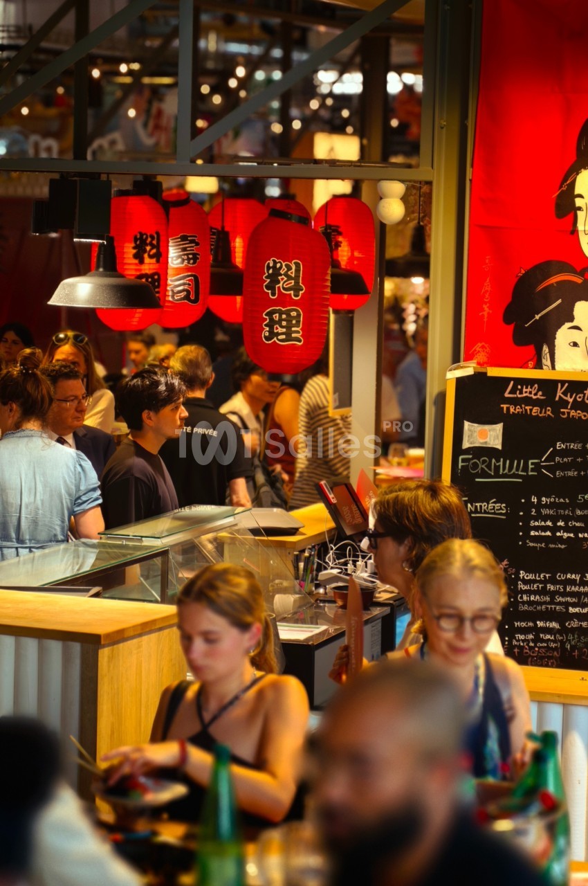 Des personnes dînent et discutent dans un restaurant animé décoré de lanternes rouges et d'affiches japonaises.